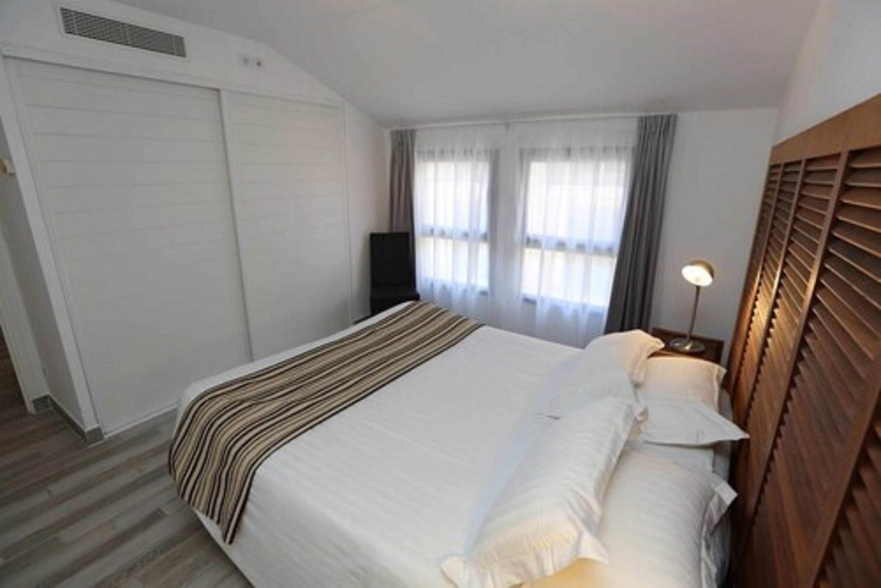 Een hotelkamer met een groot bed, een kledingkast, een televisietoestel en een bedlamp.