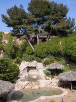 Un jardín con una formación rocosa, un estanque pequeño y sombrillas de paja.