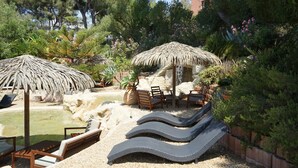 Un espace piscine comprenant des chaises longues, un parasol en chaume et un coin salon avec une table et des chaises.
