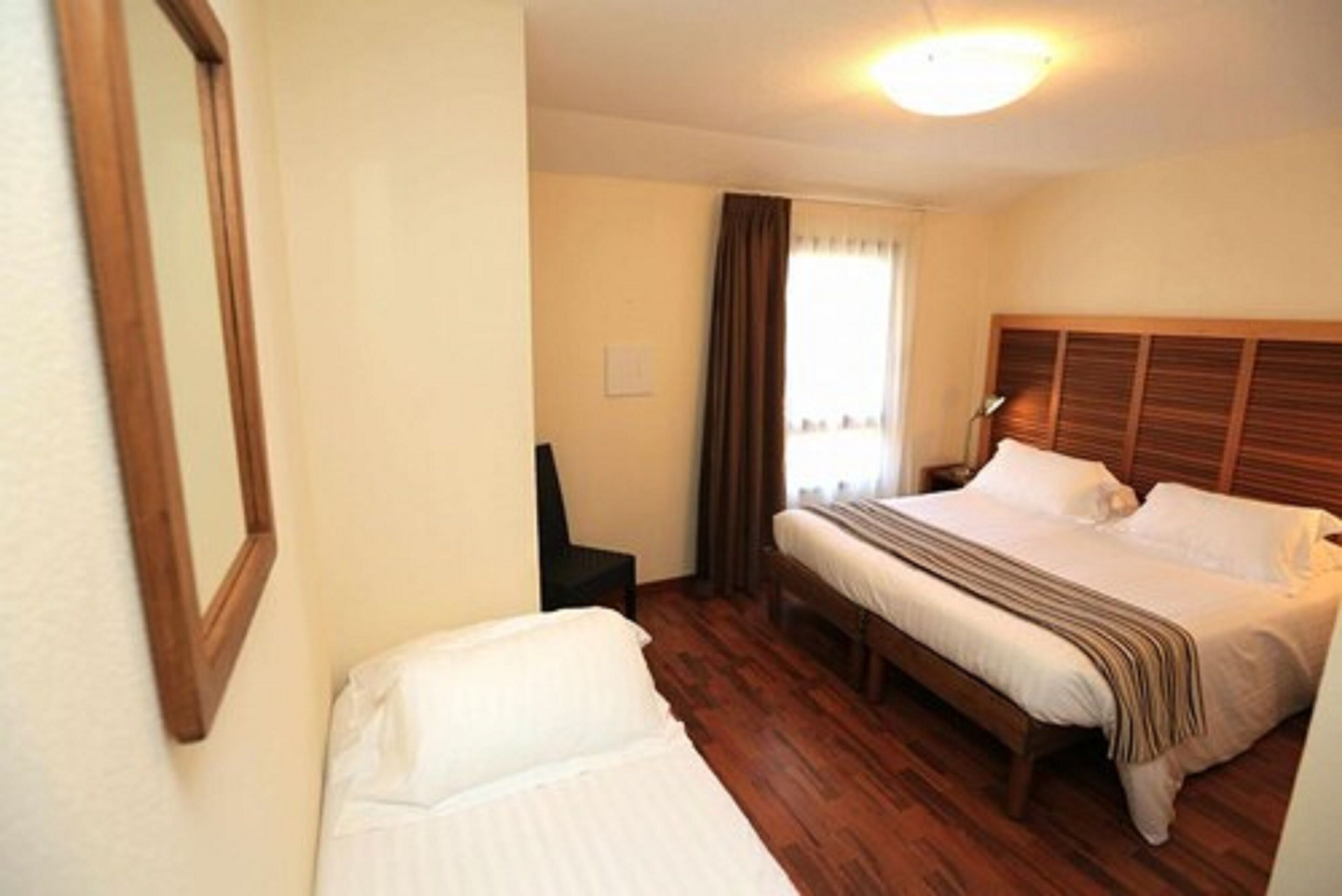 Habitación de hotel con una cama individual, una mesita de noche, una silla y una ventana con cortinas.