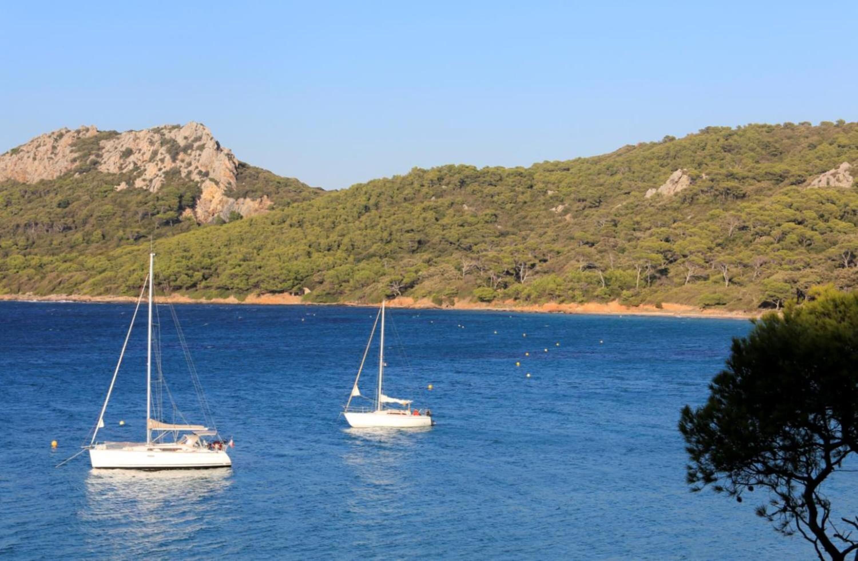 Two sailboats on calm water with a hilly landscape in the background.