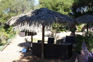 Un jardín con sombrilla de paja, mobiliario exterior y diversas plantas.