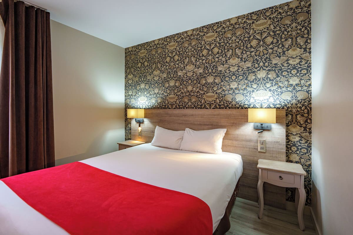 Une chambre d’hôtel avec un grand lit, une table de chevet avec deux lampes et un papier peint à motifs sur le mur.