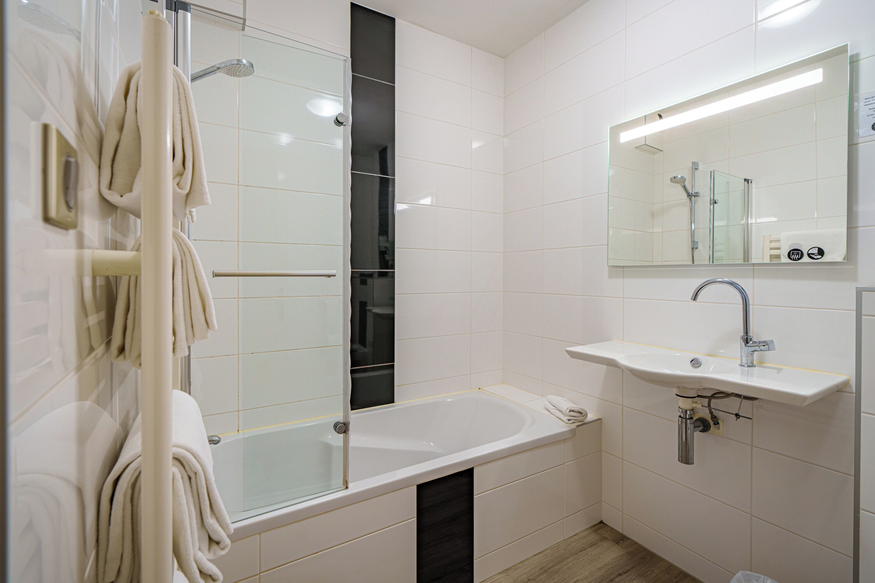 Ein Badezimmer mit einer gläsernen Duschkabine, einer weißen Badewanne und einem Waschbecken mit Spiegel.