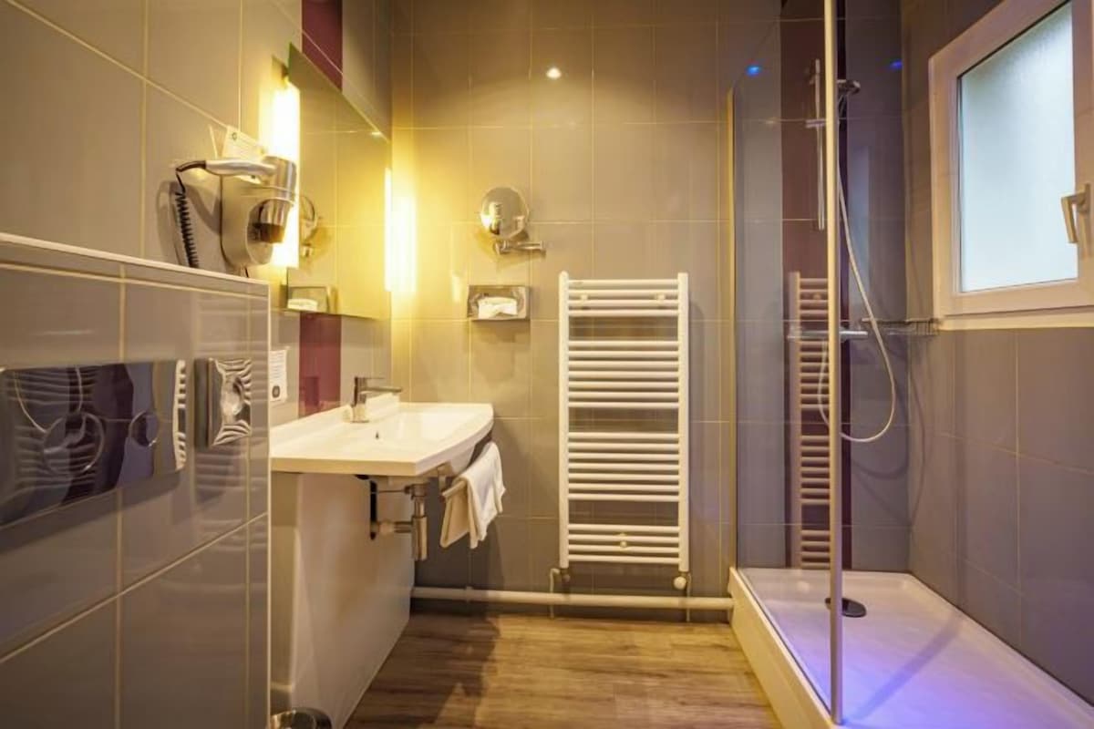 Un baño moderno con cabina de ducha de vidrio, un lavamanos blanco y un perchero para toallas.