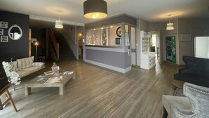 Un vaste espace de vie doté d’un plancher en bois, d’un canapé, d’une table basse avec des magazines et d’un comptoir d’accueil avec une horloge.