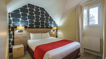 A bedroom with a sloped ceiling, a bed with a red blanket, two bedside lamps, a wooden headboard, and a window with curtains.