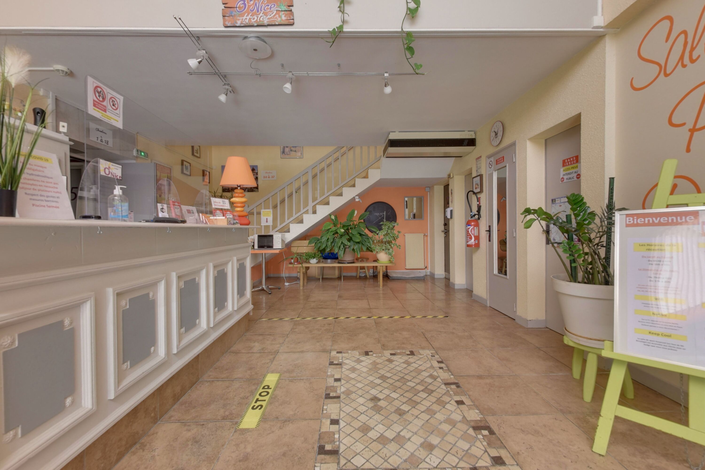 Zona de recepción de un hotel, con mostrador de recepción, una escalera y un cartel de bienvenida.
