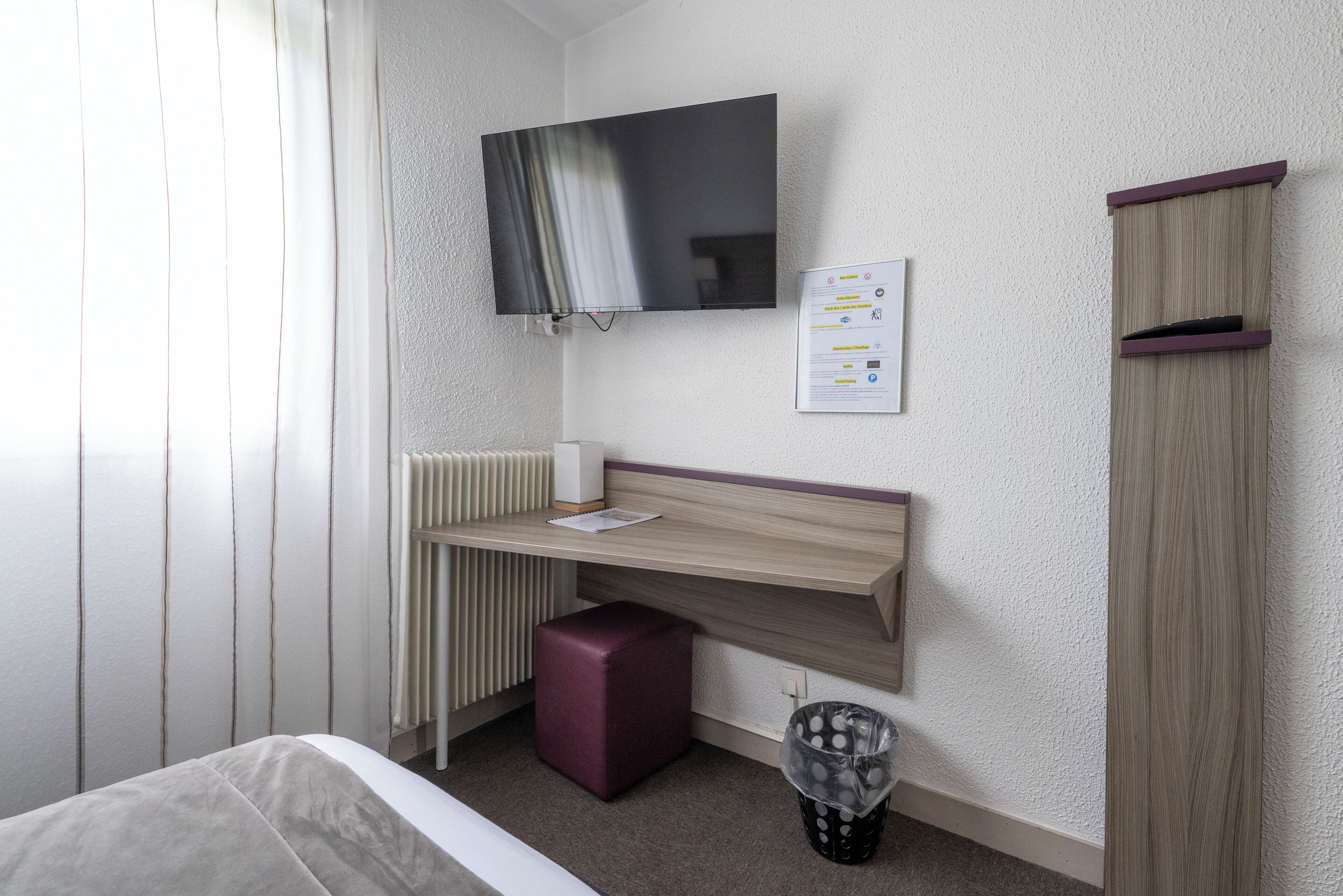 Une chambre à coucher comprenant un lit, un bureau, une télévision, un radiateur, une poubelle et une armoire.