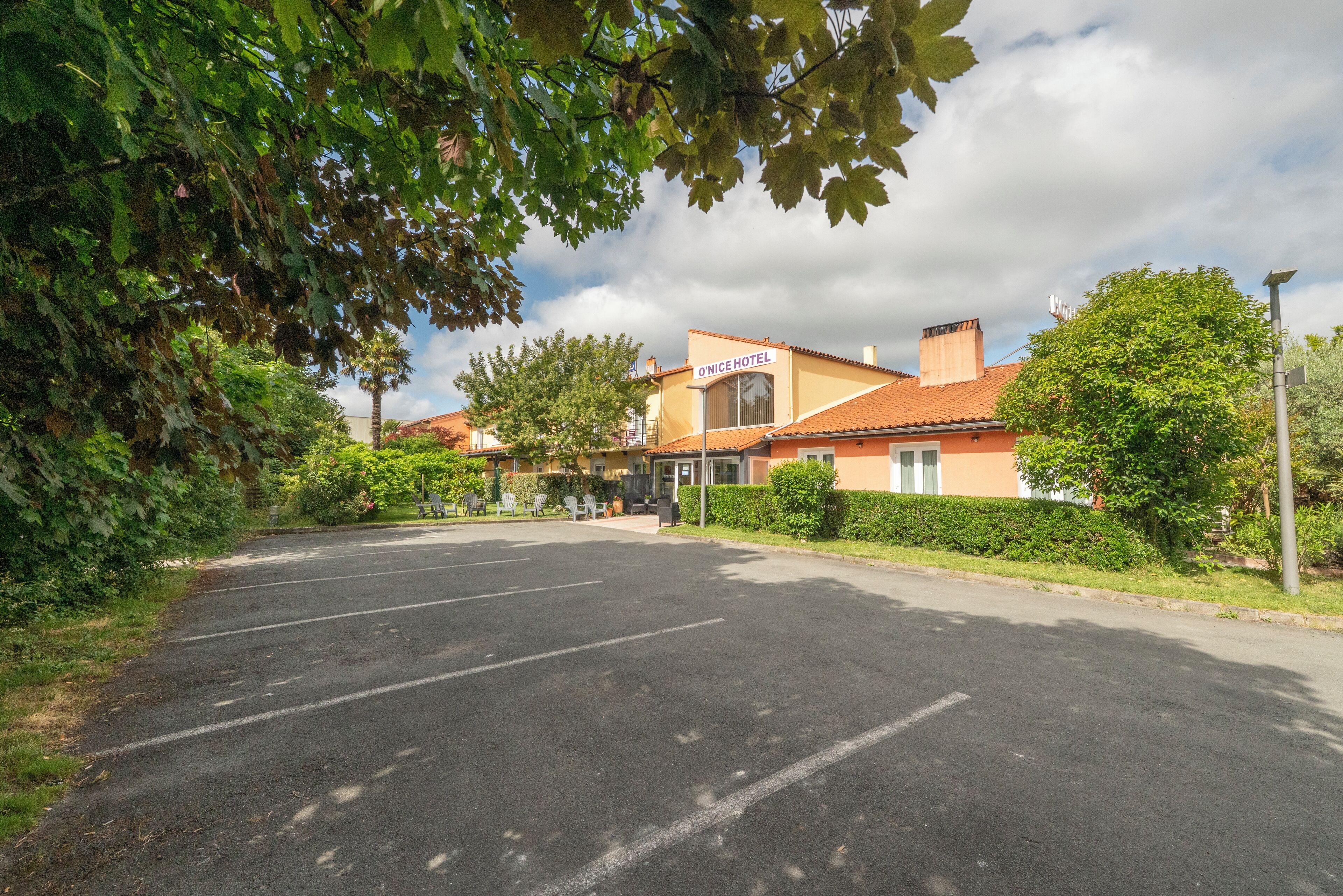 A hotel with a red-tiled roof, a sign reading "O'Nice Hotel," and a parking lot in front.