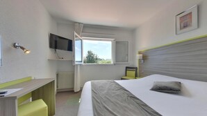 A hotel room with a bed, a desk, a chair, a television, a window, and a radiator. - Contact Hôtel O’Nice Saintes (Saintes)