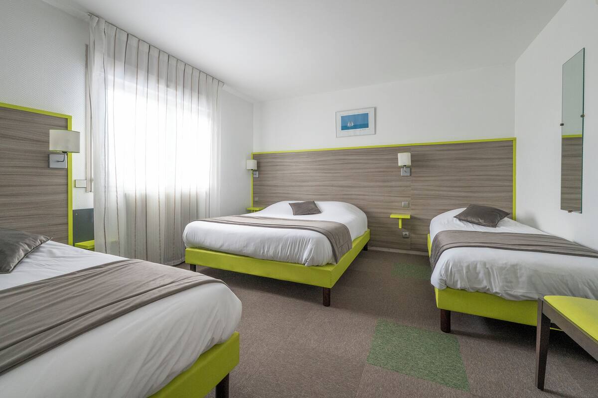 A hotel room with two beds, a green accent wall, a small table, and a window with curtains.