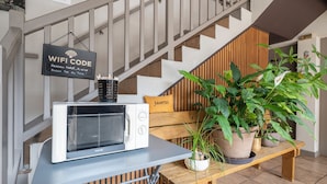 A kitchen area with a microwave on a table, a WIFI sign, and a wooden bench with potted plants. - Contact Hôtel O’Nice Saintes (Saintes)