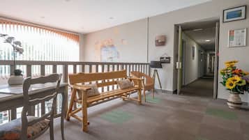 A room with a wooden bench, chairs, a desk, and a window with blinds.