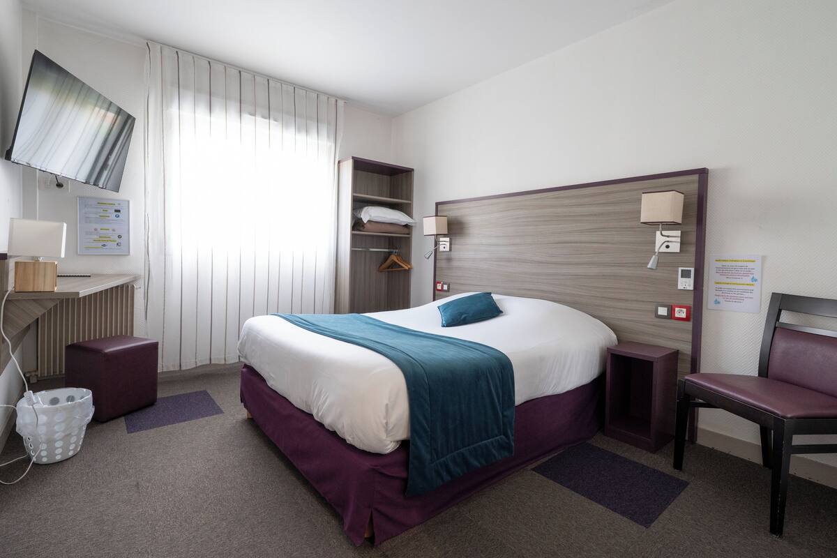 A hotel room with a bed, a desk, a chair, a TV, and a bathroom area.