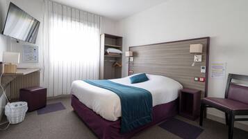 Habitación de hotel con cama, escritorio, silla, televisor y zona de baño.