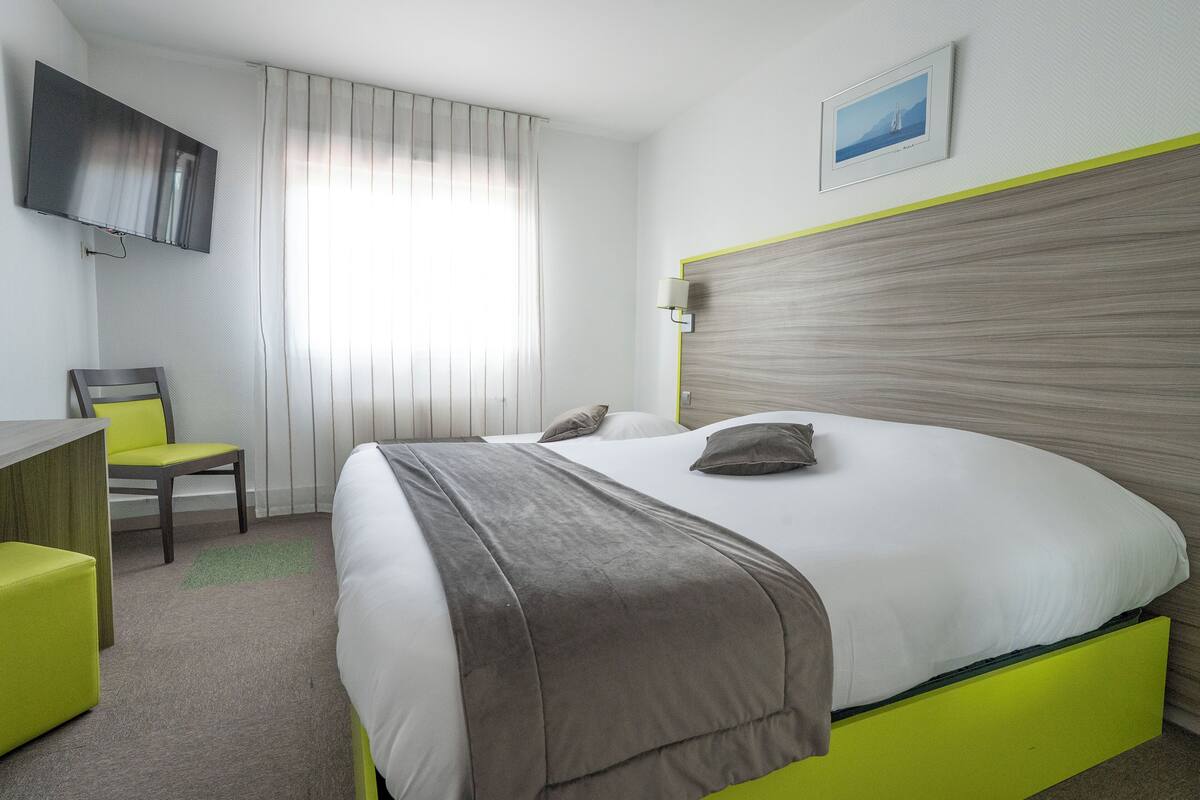 A hotel room with a bed, a desk, a chair, a TV, and a window with curtains.