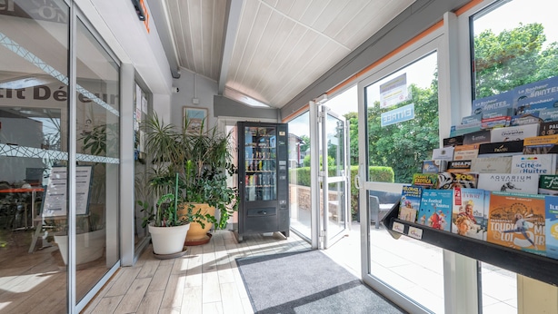A hotel entrance with a glass door, potted plants, a vending machine, and a display of travel brochures. - Contact Hôtel O’Nice Saintes (Saintes)