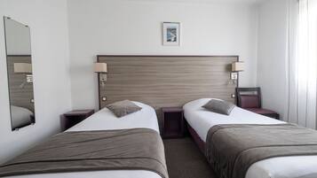 A hotel room with two beds, a wooden headboard, bedside tables with lamps, a framed picture on the wall, and a window with curtains.