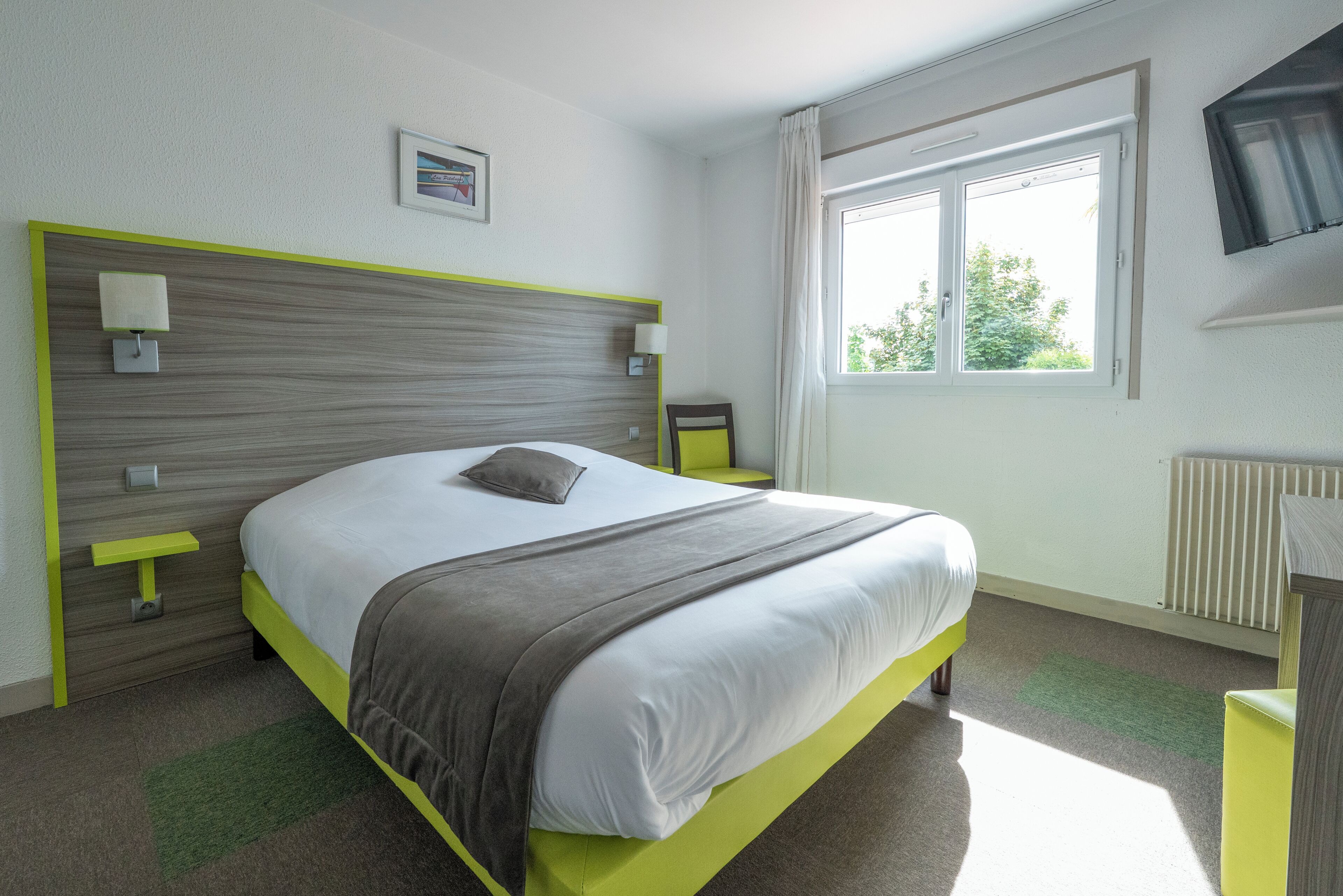 A modern hotel room with a large bed, bedside lamps, a window with a view, and a flat-screen TV.