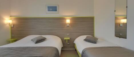 A hotel room with two single beds, a wooden headboard, bedside lamps, a small table, and a framed picture on the wall.