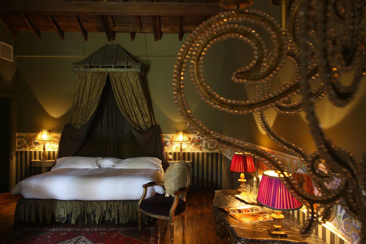 A bedroom with a canopy bed, two bedside lamps, a chair, and a small table with a lamp.