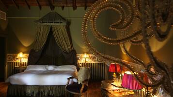 A bedroom with a canopy bed, two bedside lamps, a chair, and a small table with a lamp.