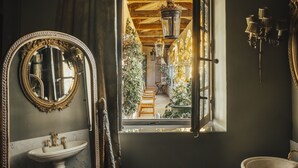 Et badeværelse med et stort spejl, en vask, et vindue der giver udsigt til en have, og en lysekrone.