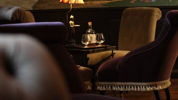 A room with a large mural depicting a historical scene, a table with a lamp, and two plush armchairs.