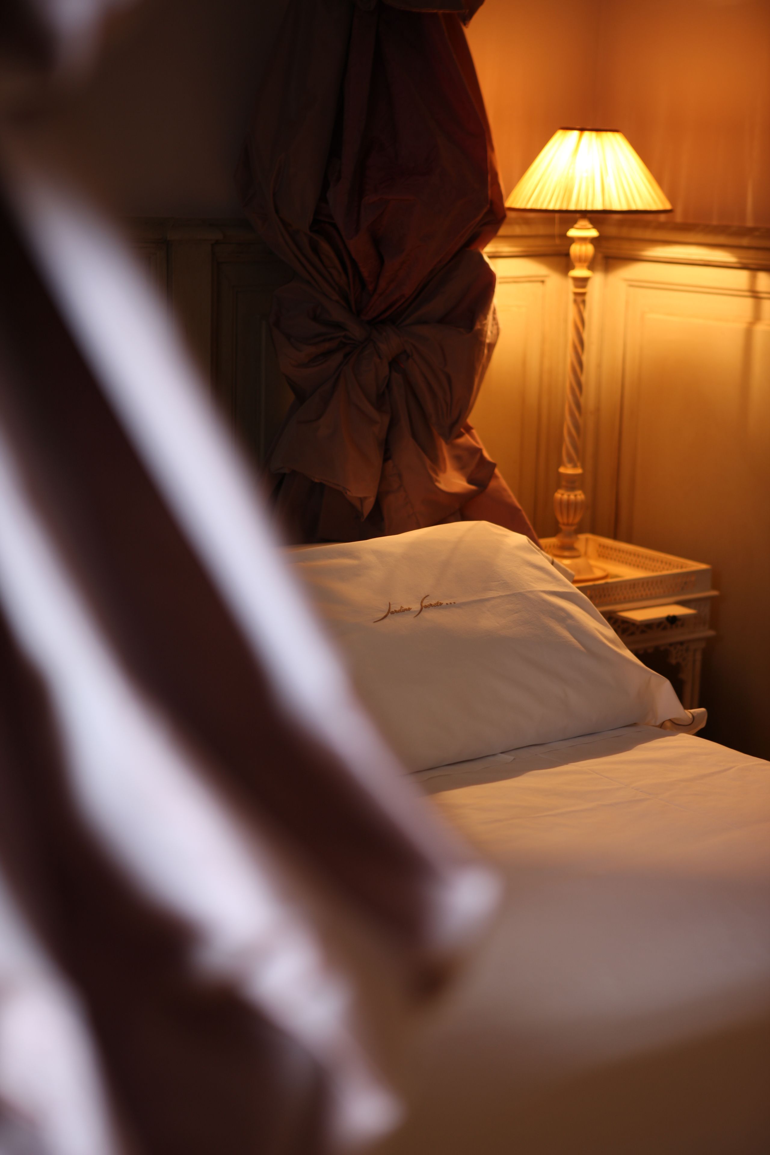 A bed with a white pillow and a lamp on a bedside table.