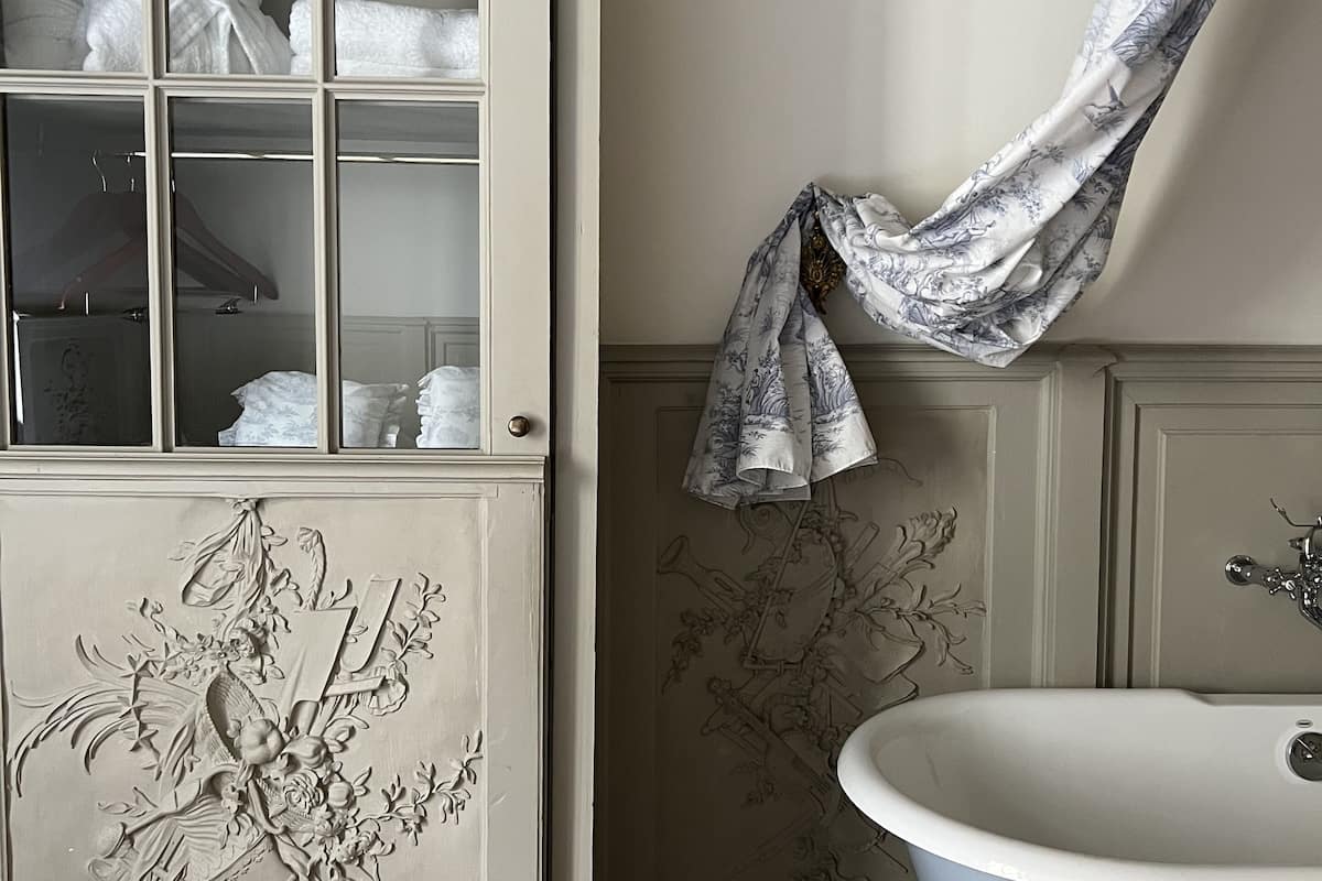 A bathroom with a freestanding bathtub, a glass-fronted cabinet with towels, and a floral wall panel.