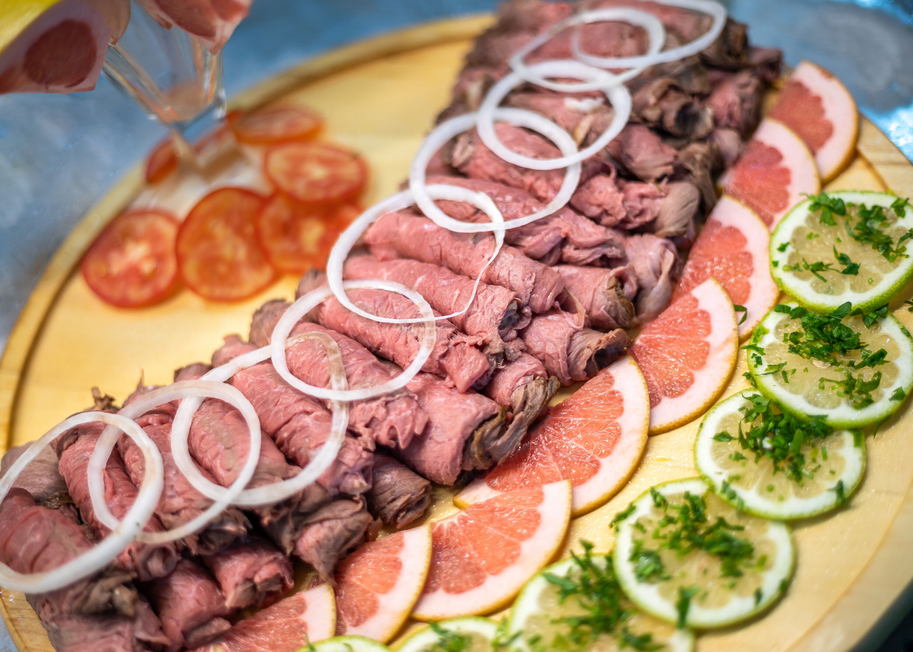 Una bandeja con carne de res en rodajas, tomates, cebollas y frutas cítricas.