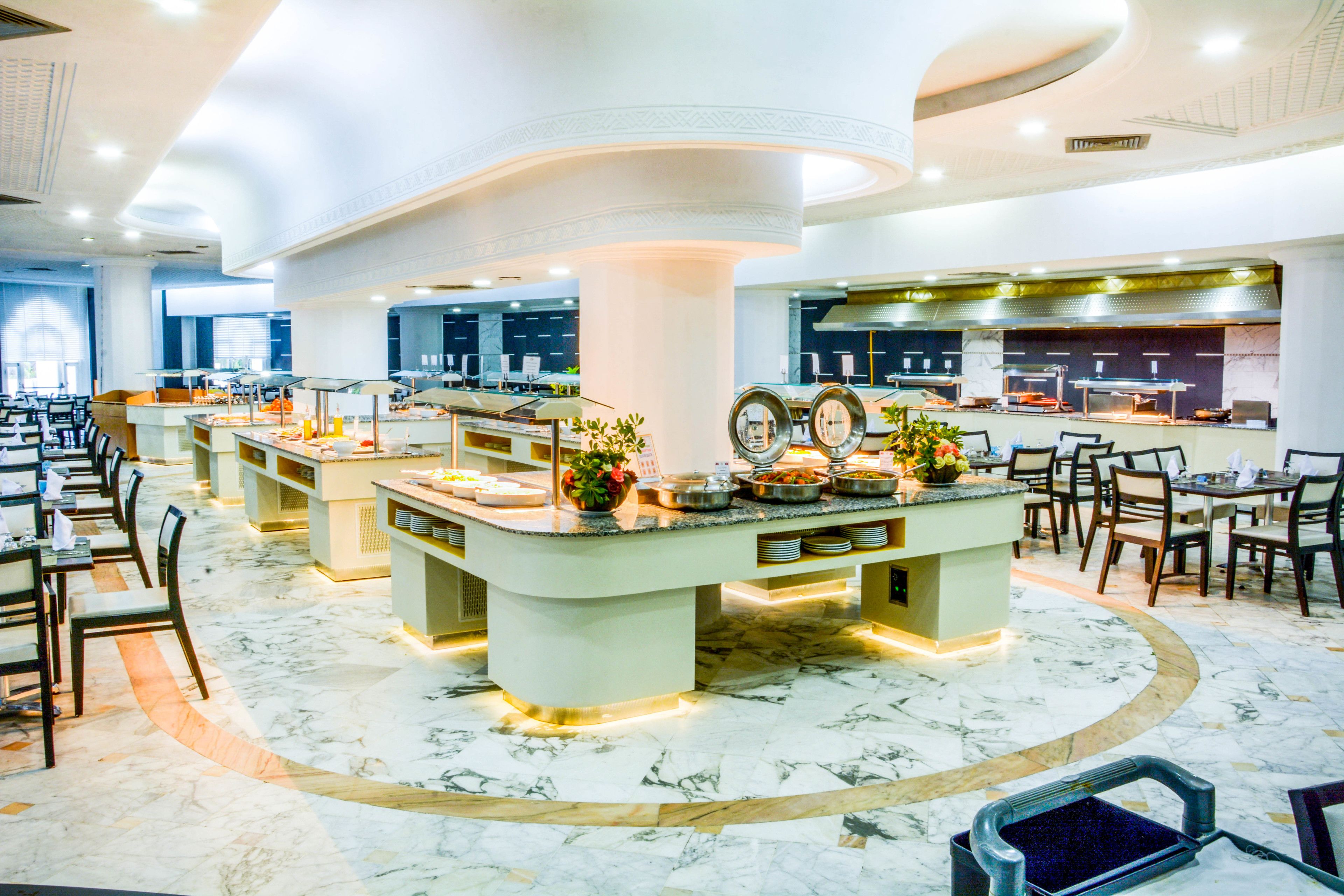 Un hall de hotel espacioso con varias zonas de restauración, un bar central y un suelo de mármol.