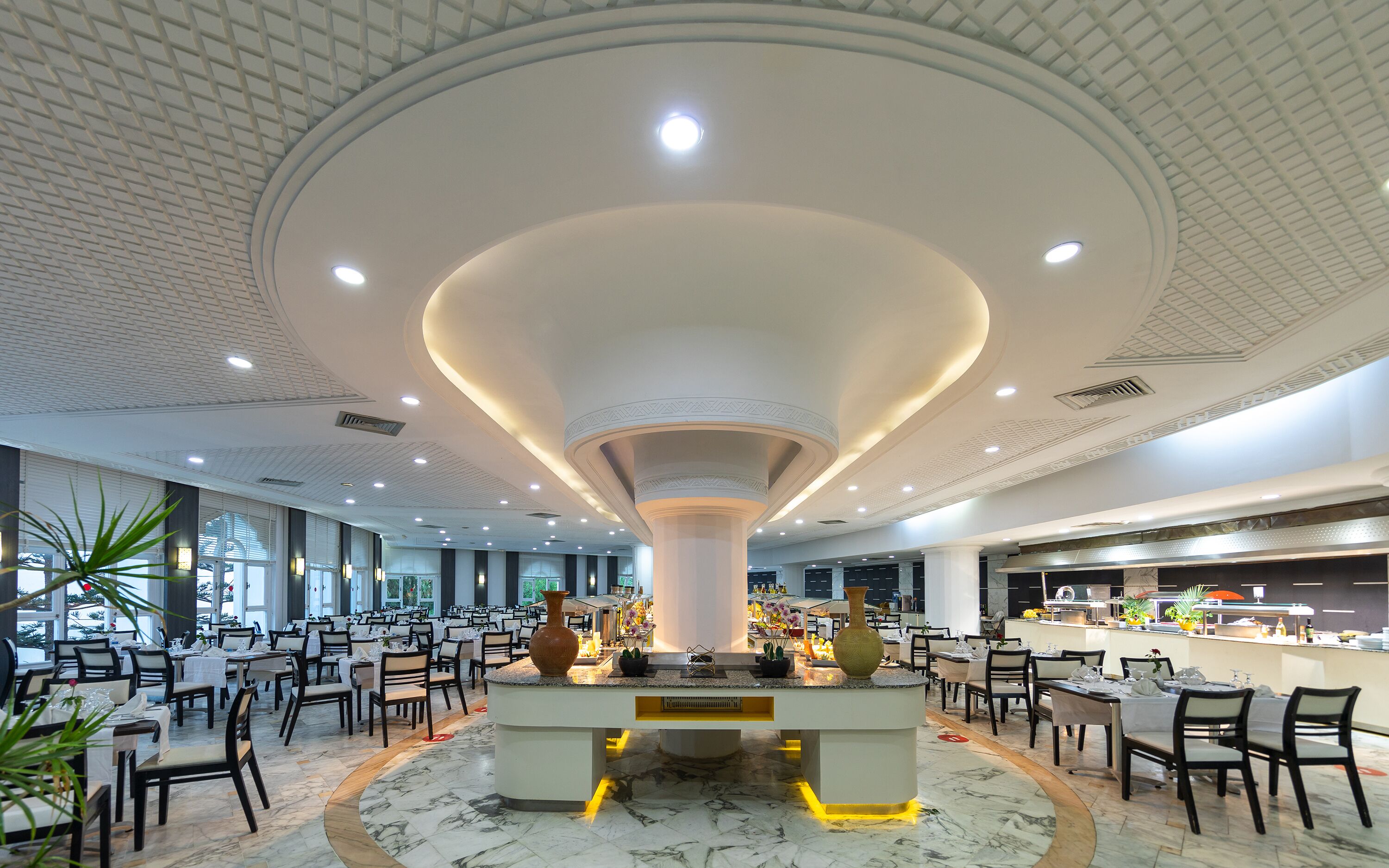 Un vaste espace dédié à la salle à manger, avec un îlot central, plusieurs tables et des chaises disposées autour.