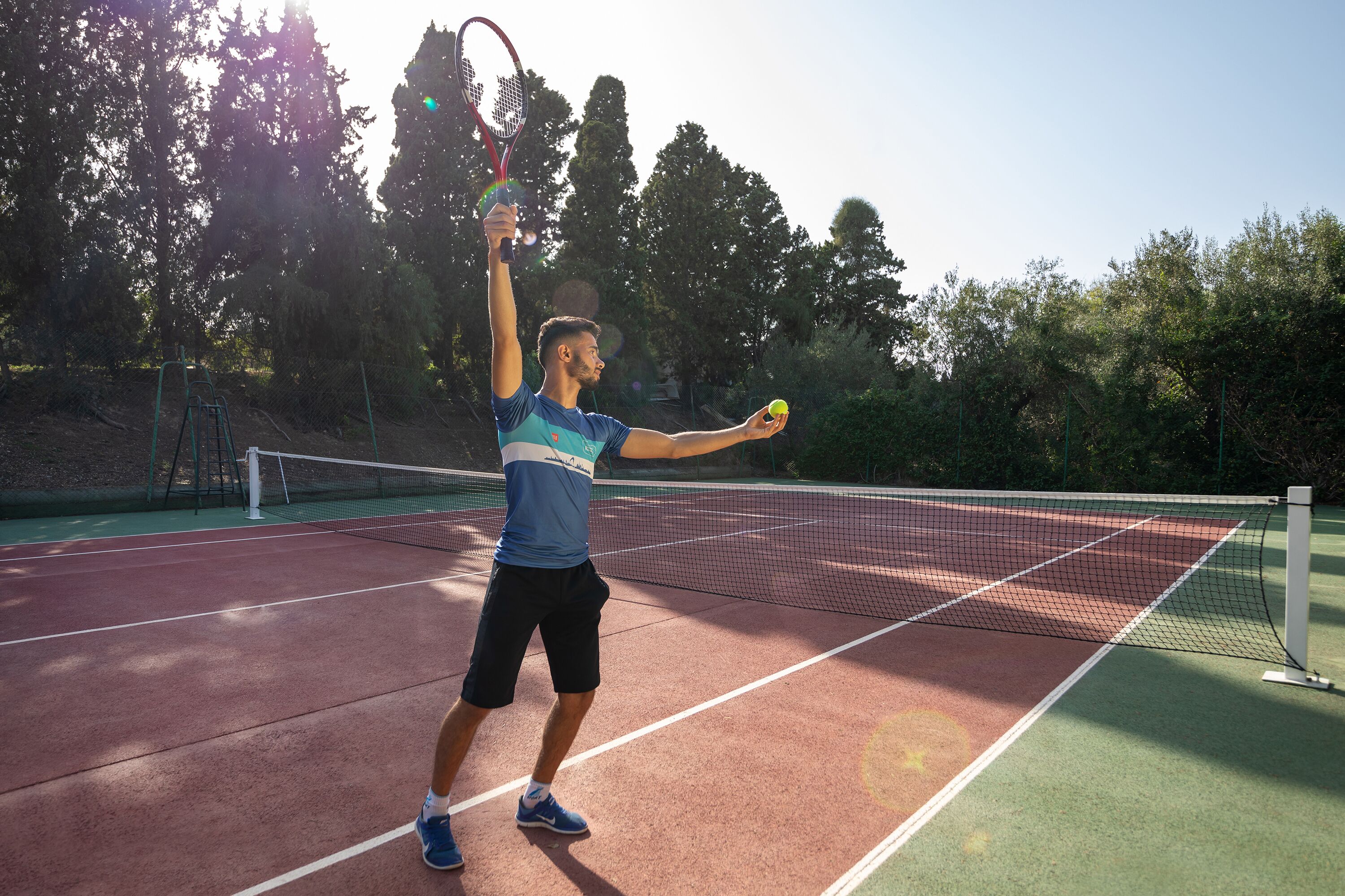 A tennis court with a net, trees, and a clear sky.