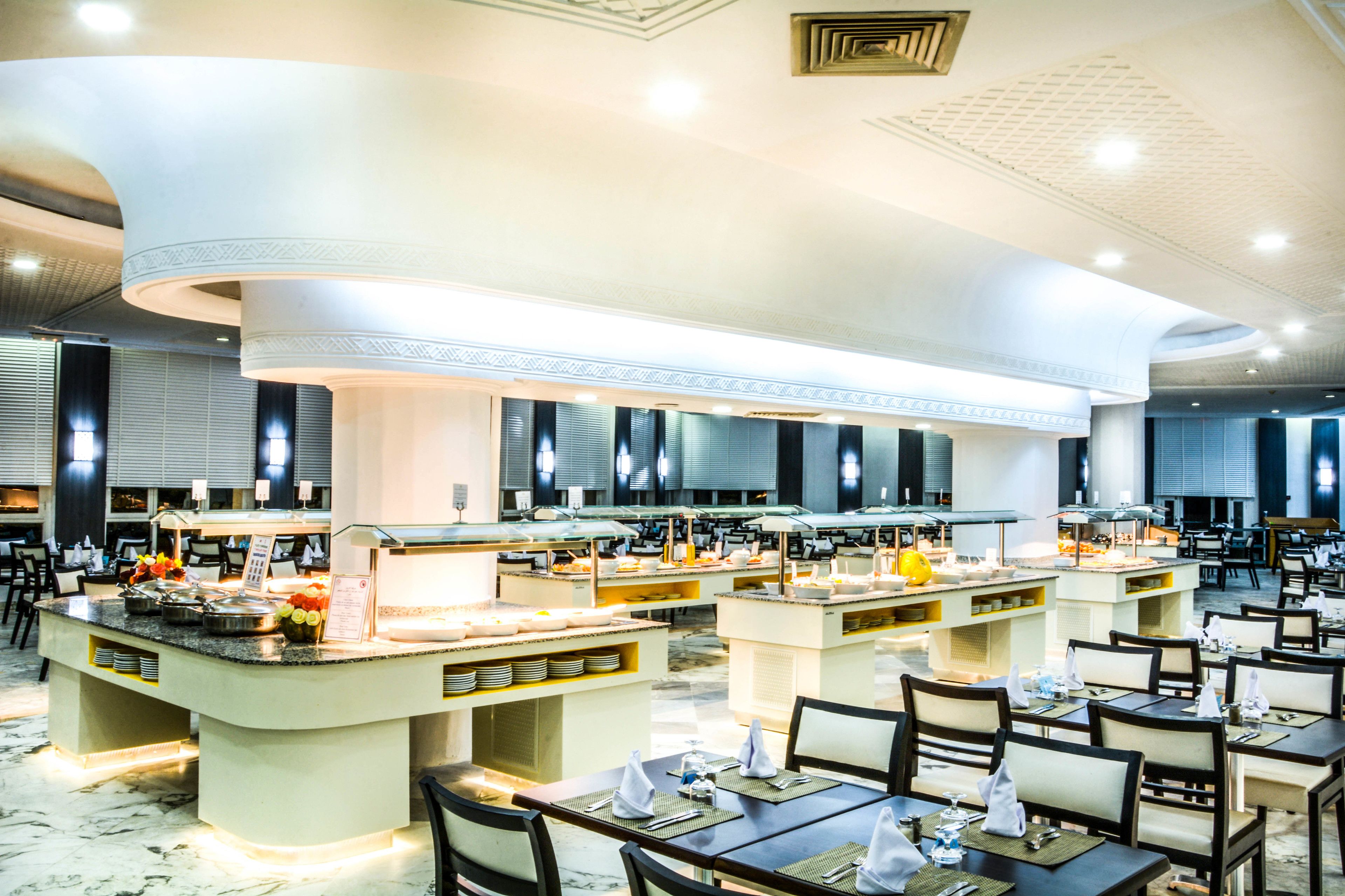 A spacious hotel dining area with multiple seating arrangements and a central buffet station.