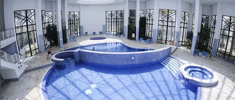 Una piscina techada, una piscina al aire libre, sombrillas