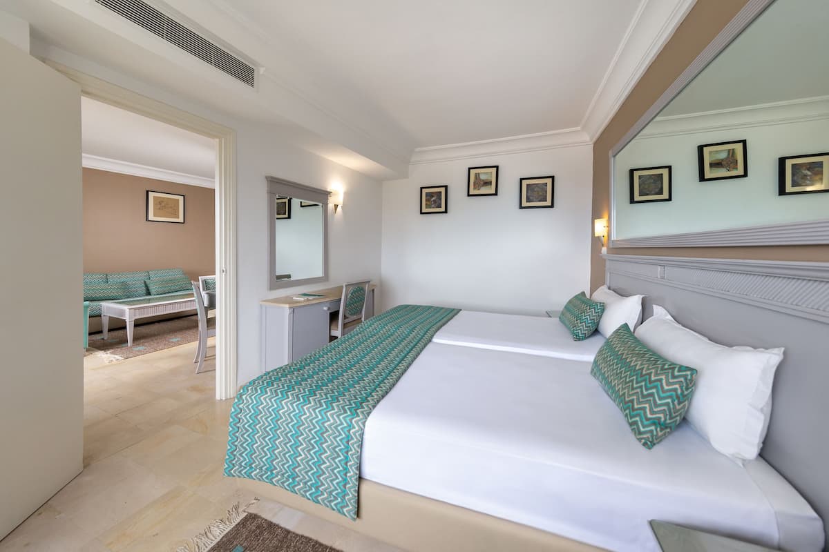 Habitación de hotel con dos camas, un escritorio, una silla, un espejo y cuadros en la pared.