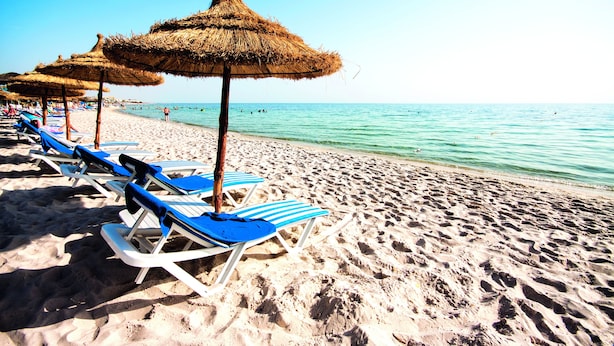 Een strand met rijen blauwe en witte ligbedden en rieten parasols.