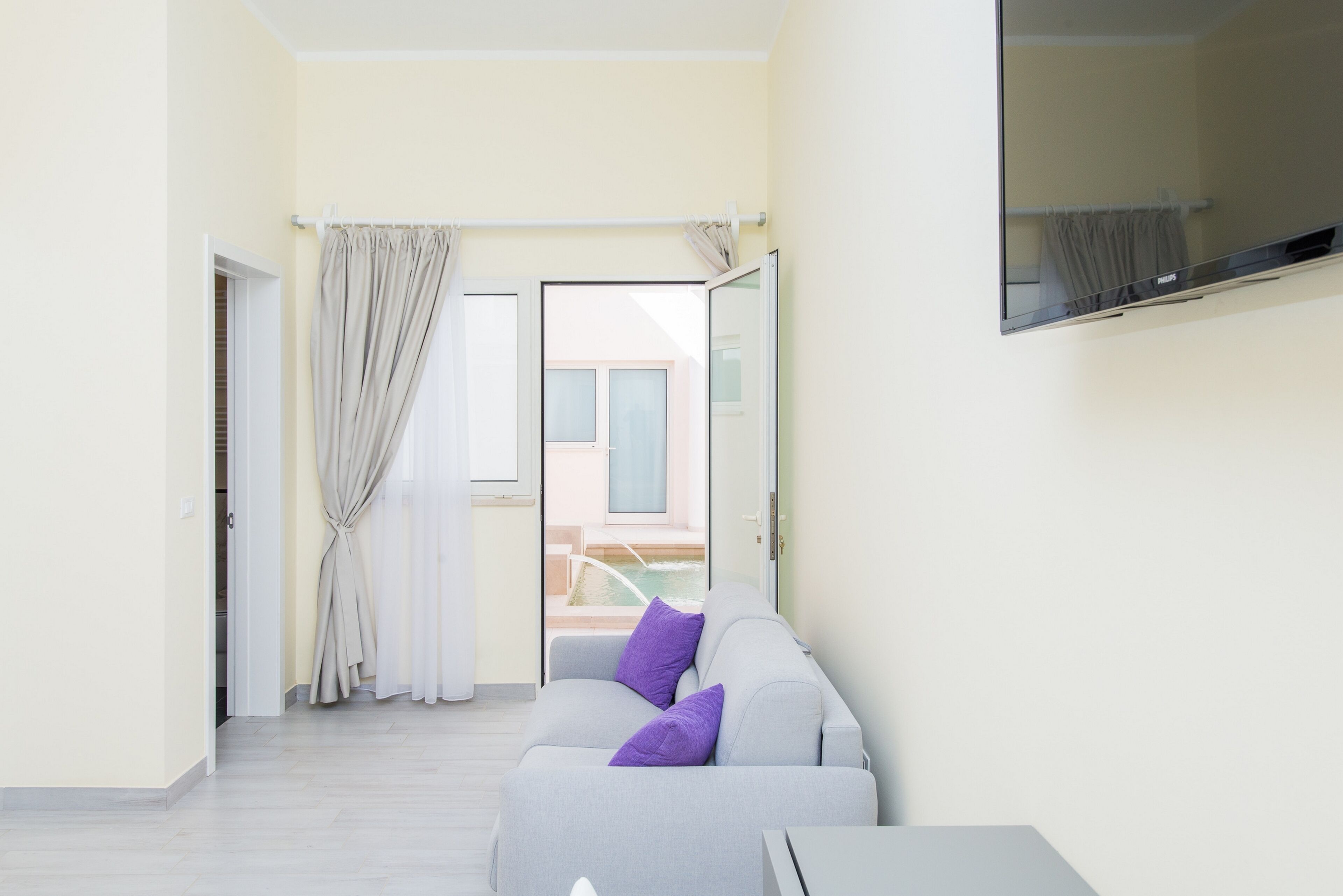 A modern living room with a grey sofa, a small table, and a view of an outdoor area through a sliding door.