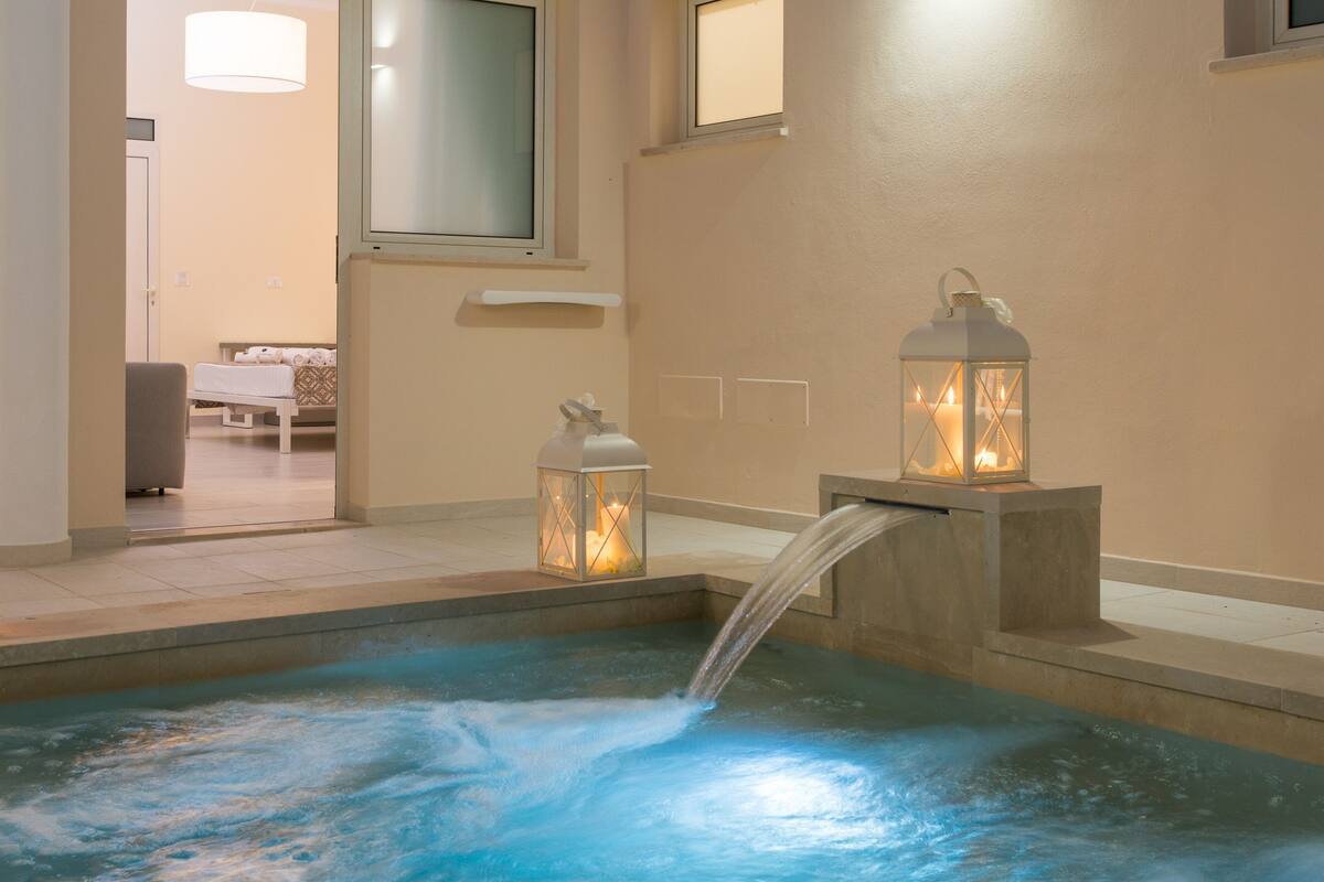 Ein Wellnessbereich mit Whirlpool, zwei beleuchteten Laternen und Blick auf ein Schlafzimmer.