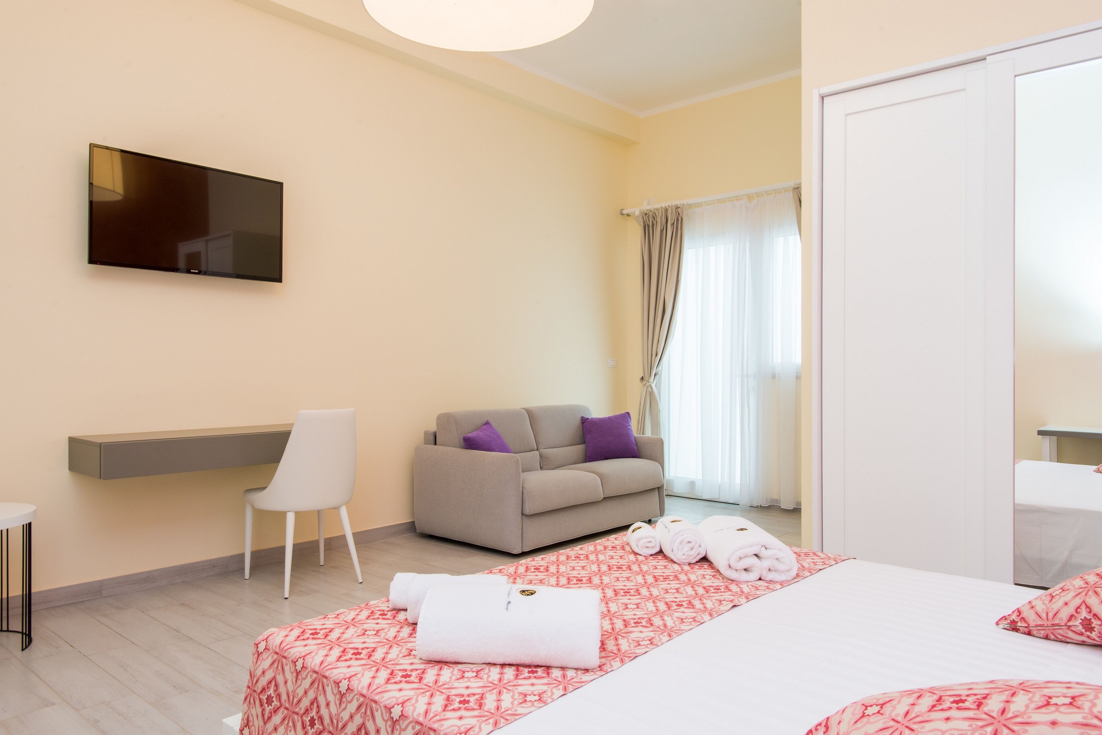 Ein Hotelzimmer mit Bett, Sofa, Fernseher, Schreibtisch und Stuhl.