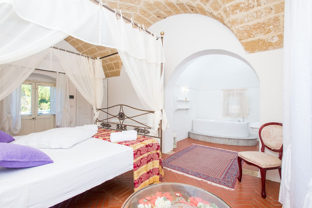Ein Schlafzimmer mit Bett, Sessel, Badewanne und Fenster.