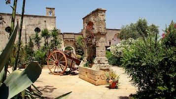 An outdoor courtyard with a stone archway, a large wooden wheel, and potted plants.