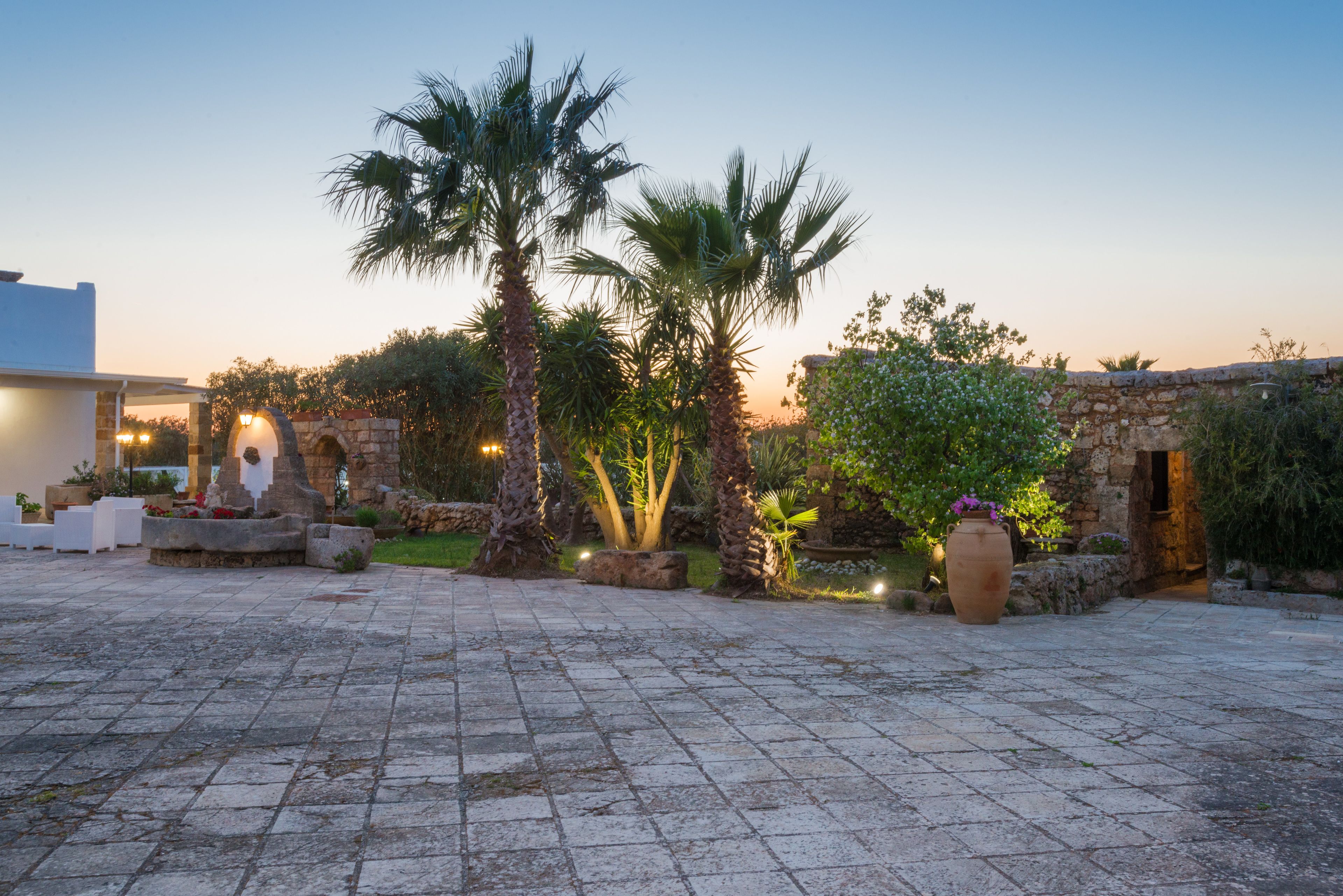 A courtyard with stone flooring, palm trees, and a large pot.