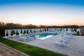 A rectangular swimming pool with white lounge chairs and umbrellas, surrounded by a paved deck and a grassy area. - Relais Masseria Casina Dei Cari (Presicce-Acquarica)