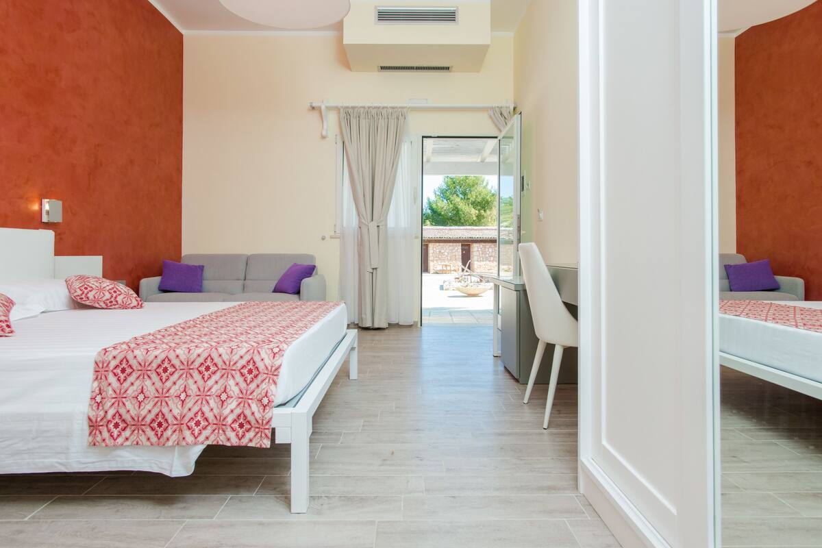 Ein Schlafzimmer mit Bett, Schreibtisch und Stuhl. Ein Fenster mit Vorhängen bietet einen Blick nach draußen.
