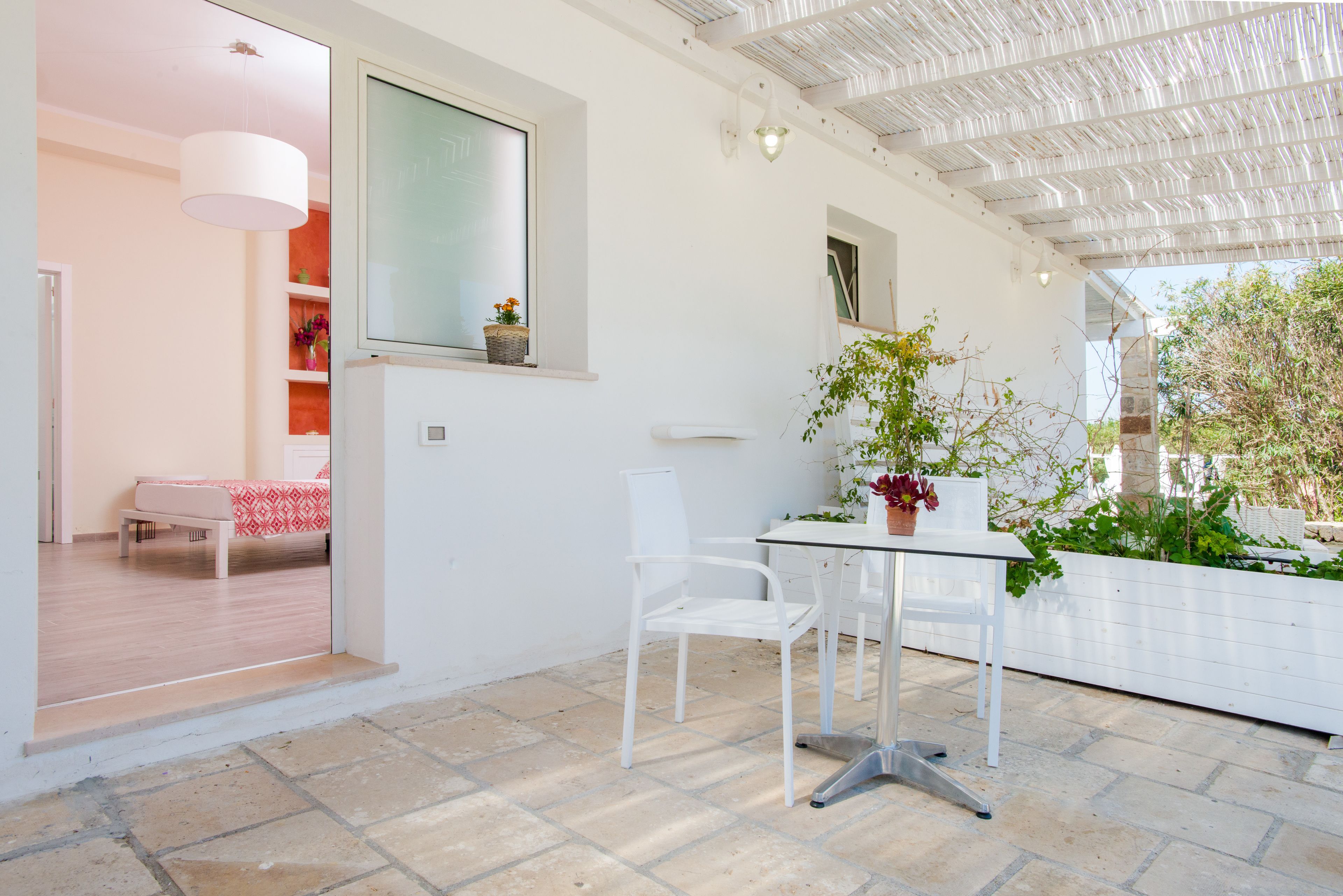 Un patio moderno con una mesa y sillas blancas, una planta en maceta y vistas del jardín.