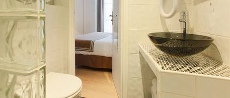 Un baño con cabina de ducha de vidrio, lavabo de vidrio y un inodoro.
