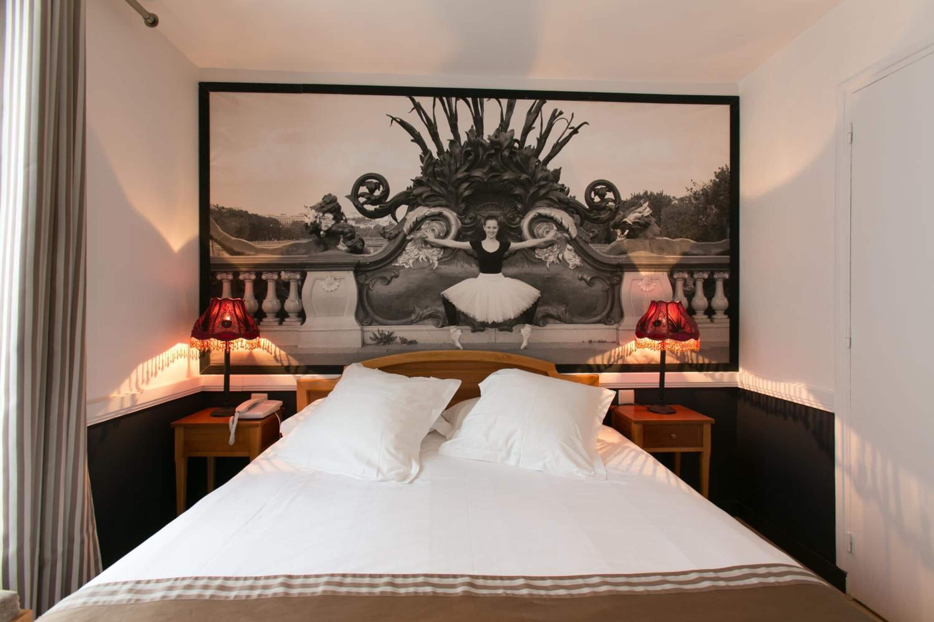 Habitación de hotel con una obra de arte grande enmarcada sobre la cama, dos lámparas de noche y un cabecero de madera.